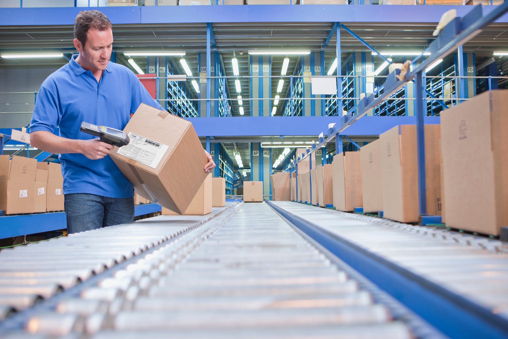 Distribution warehouse worker with barcode scanner checking durable goods packages on automated conveyor system showcasing inventory control operations