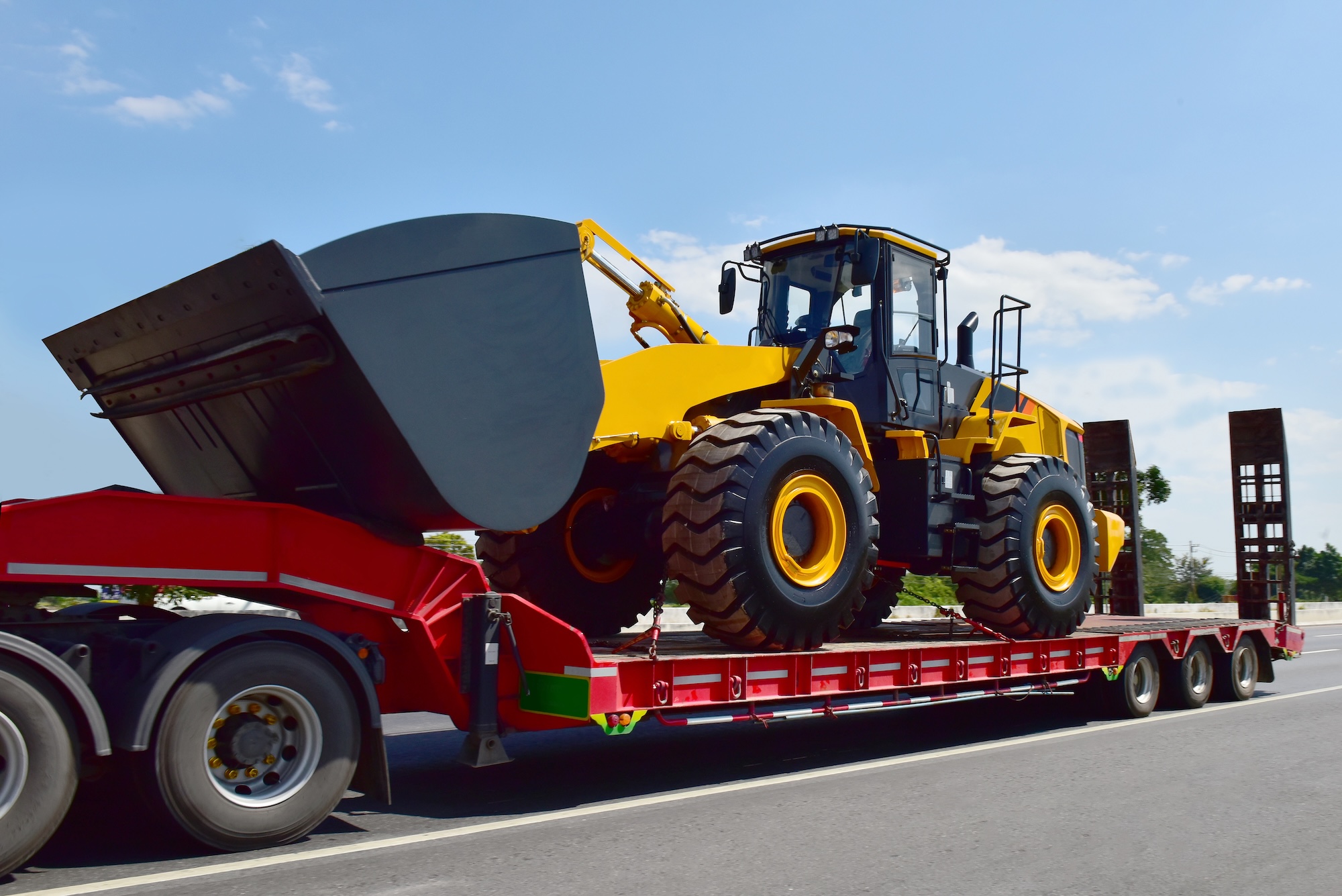 Yellow wheel loader on red flatbed trailer representing equipment rental logistics and heavy machinery transportation