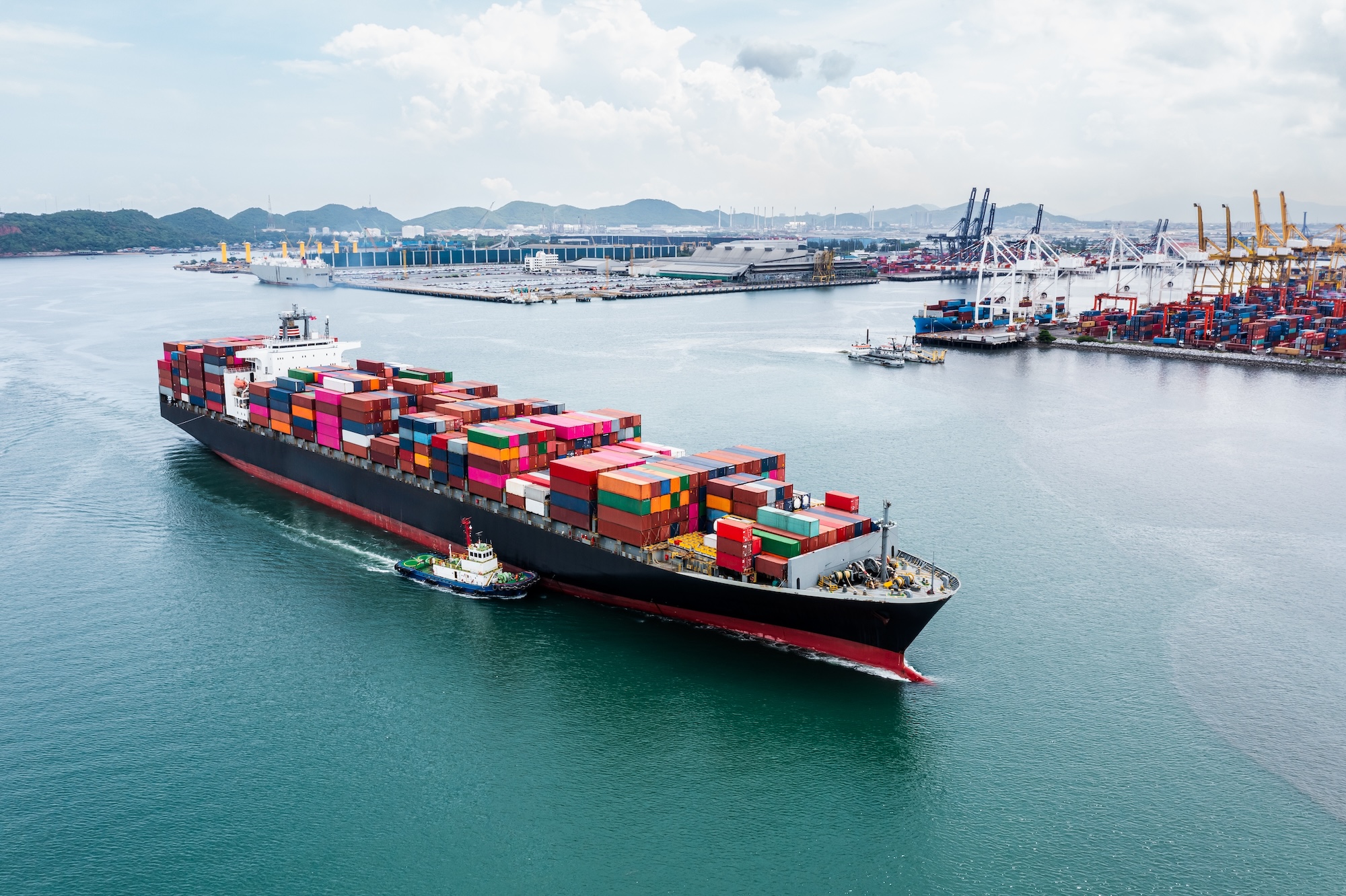 Container cargo ship with tugboats in port for logistics management. Logistics management software for supply chain optimization with container cargo ships