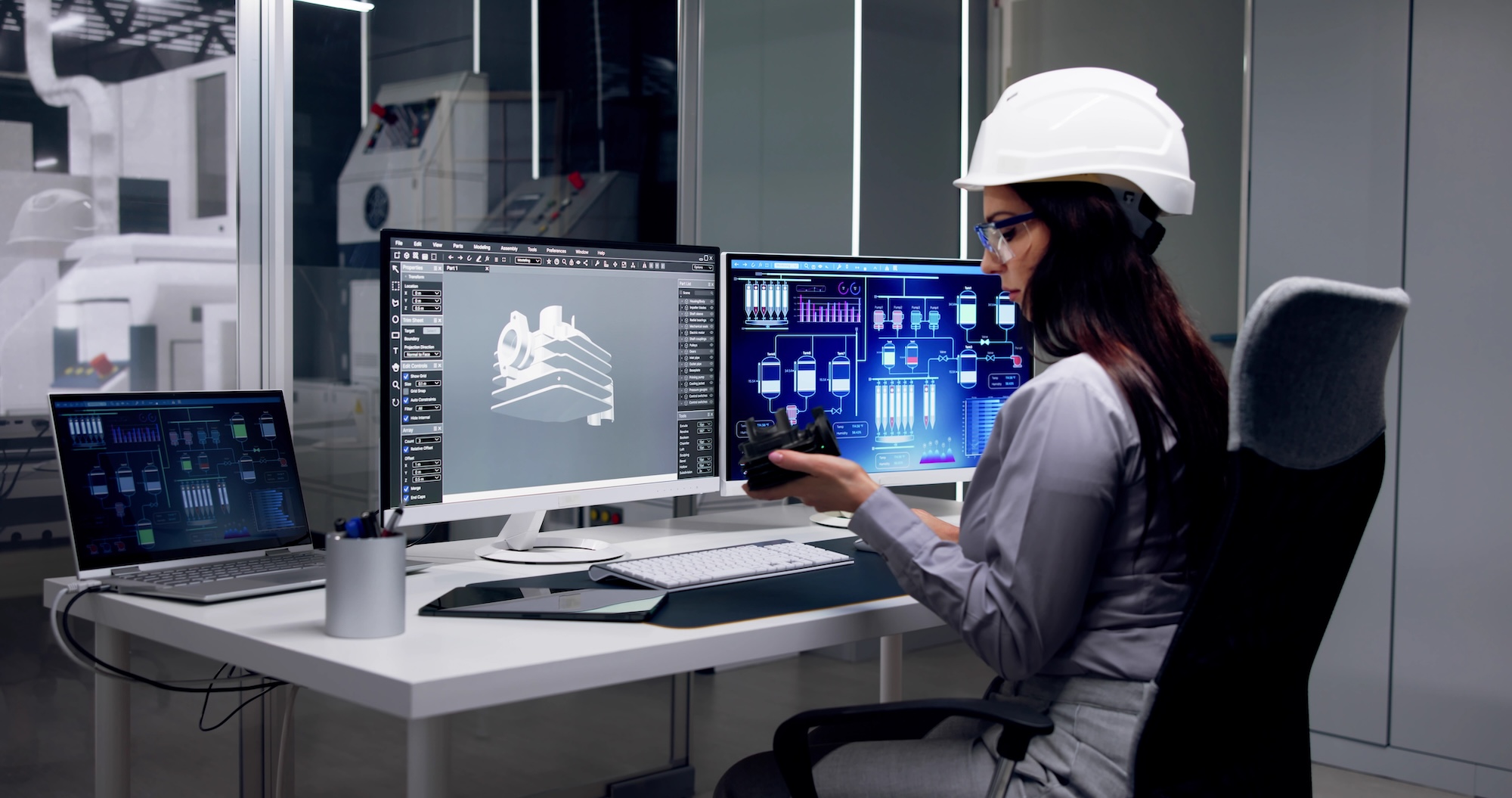 Female engineer in hard hat at modern manufacturing control station with CAD design and process control monitors for made-to-order manufacturing