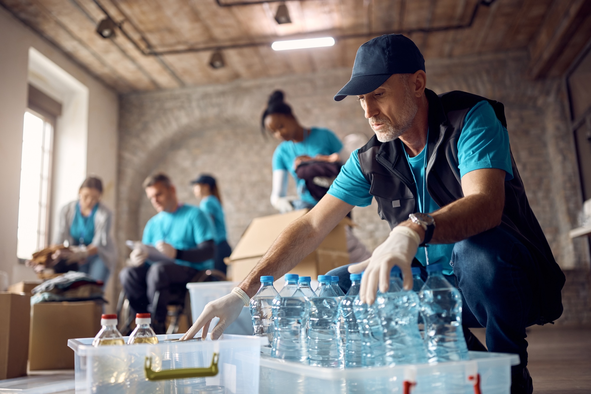 Volunteers organizing humanitarian aid supplies and water bottles for disaster relief operations. Professional nonprofit volunteers in turquoise uniforms coordinating disaster relief supplies showcasing community service and humanitarian aid