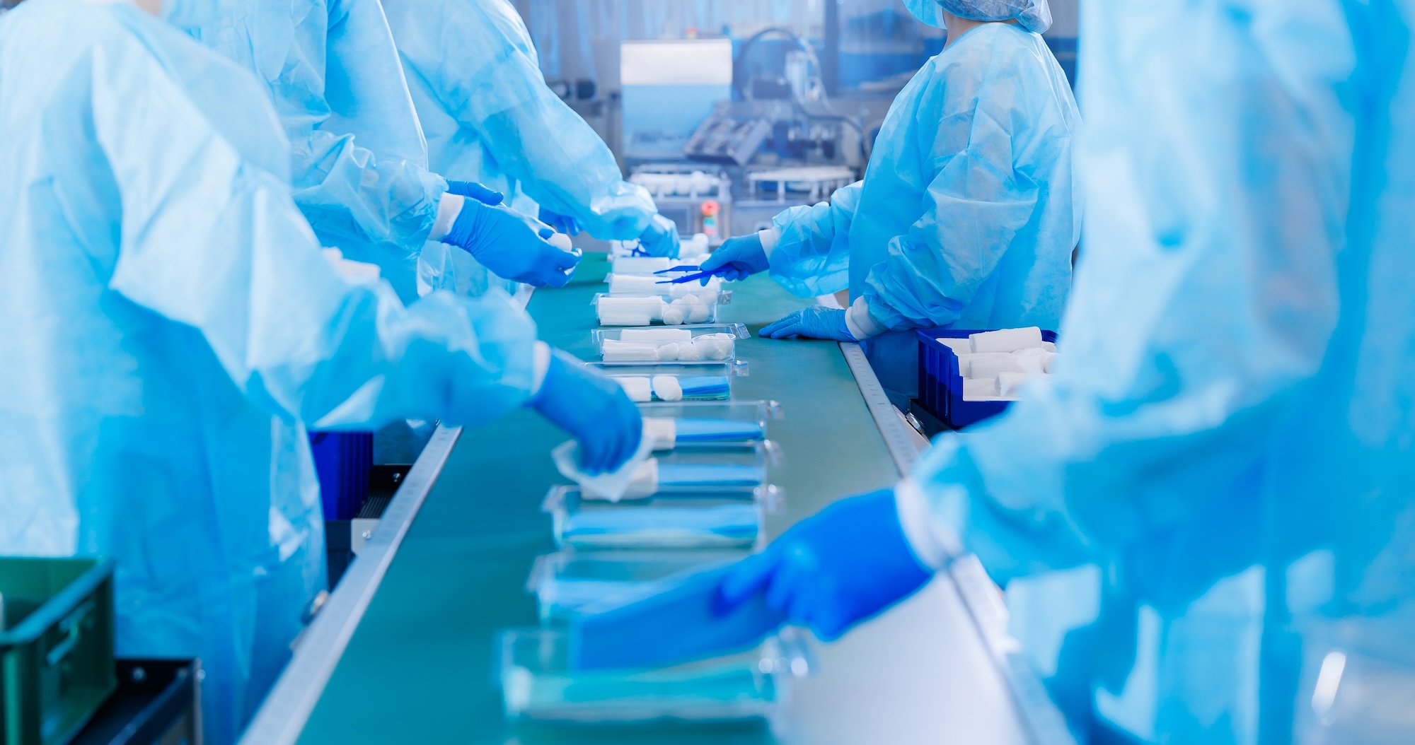 Pharmaceutical and medical device cleanroom workers in blue scrubs with hair nets operating automated production and bottling line showcasing regulatory compliance and quality control