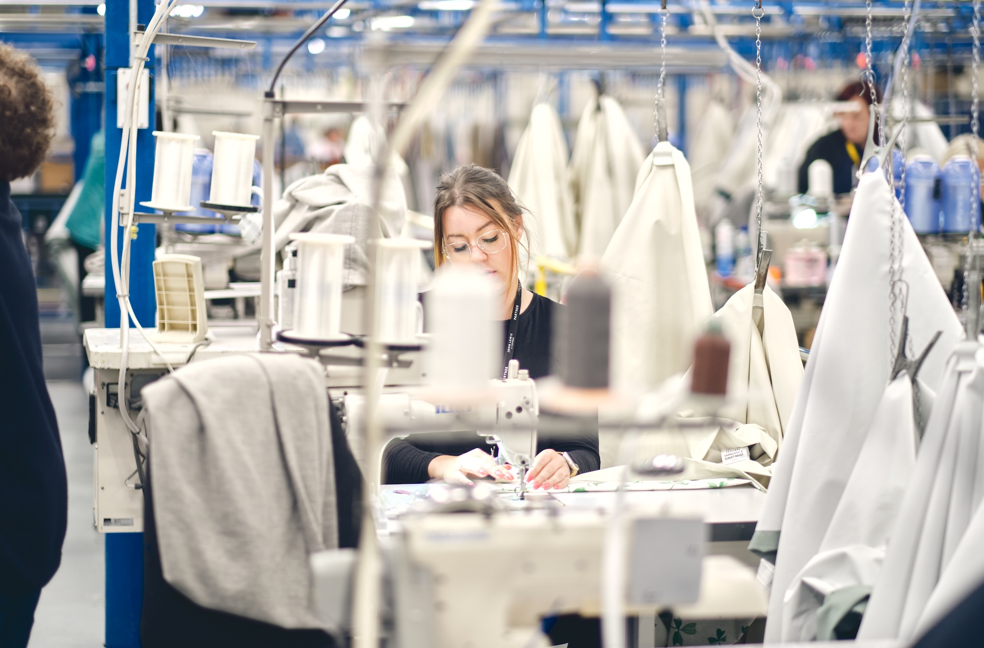 Textile and apparel manufacturing worker at sewing machine in production facility. Professional textile worker operating industrial sewing machine in modern apparel manufacturing facility showcasing production operations